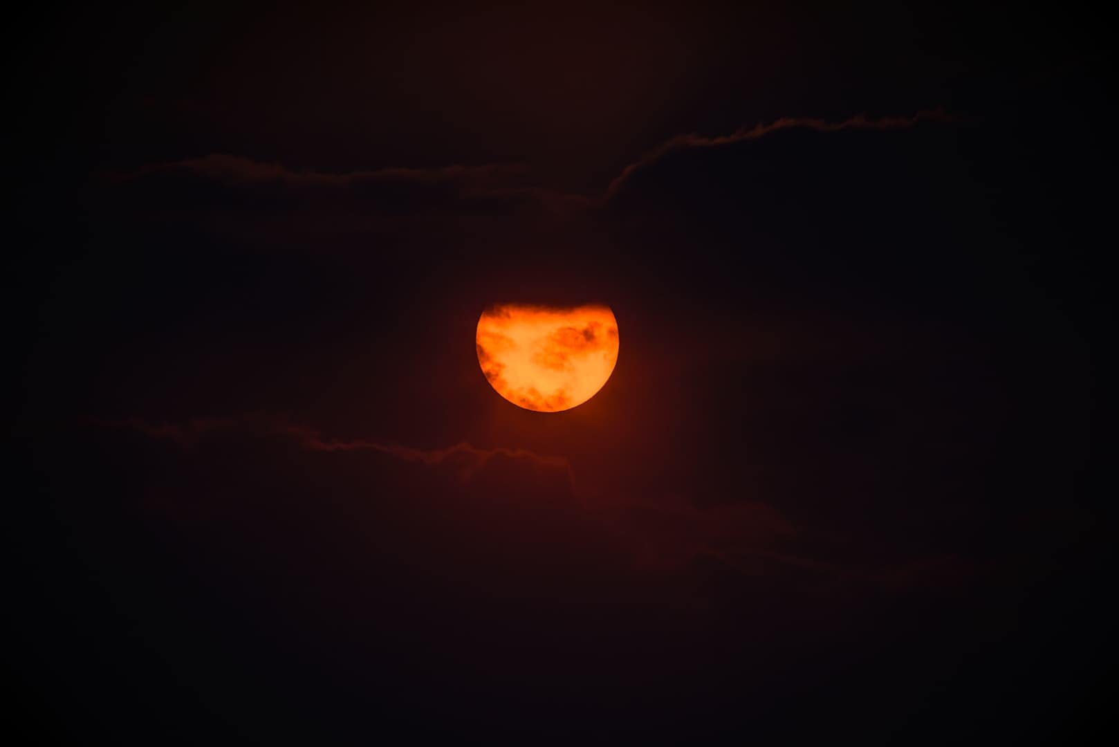 Puesta de sol ardiente con nubes oscuras rodeando el sol en un cielo profundamente contrastado. Fotografía de Ignacio Arcas Almudí